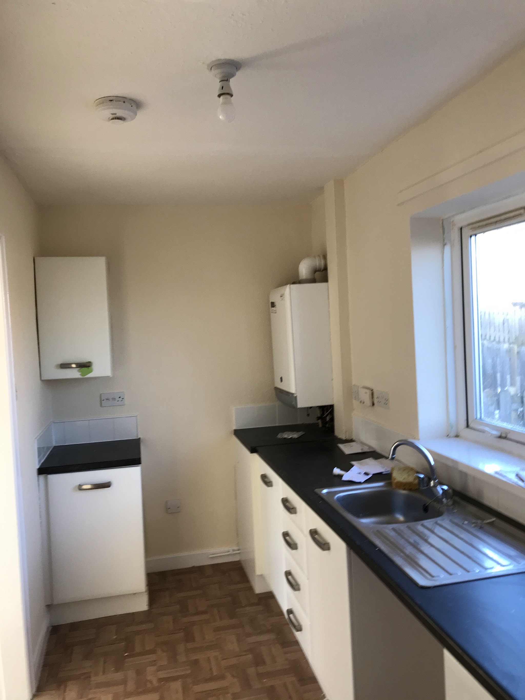 Freshly decorated galley kitchen with cream walls, white units and a dark worktop