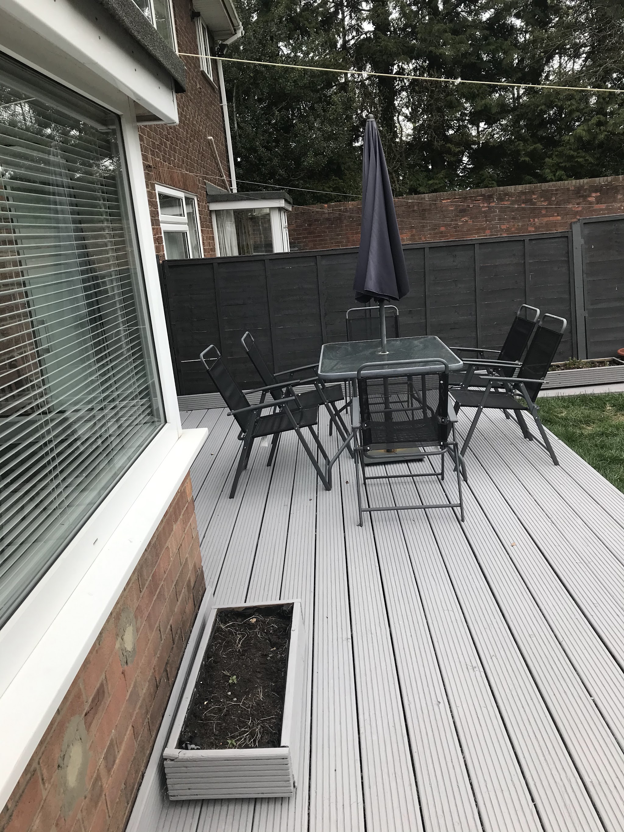 Pale grey decking with a garden table and chairs beside a white window