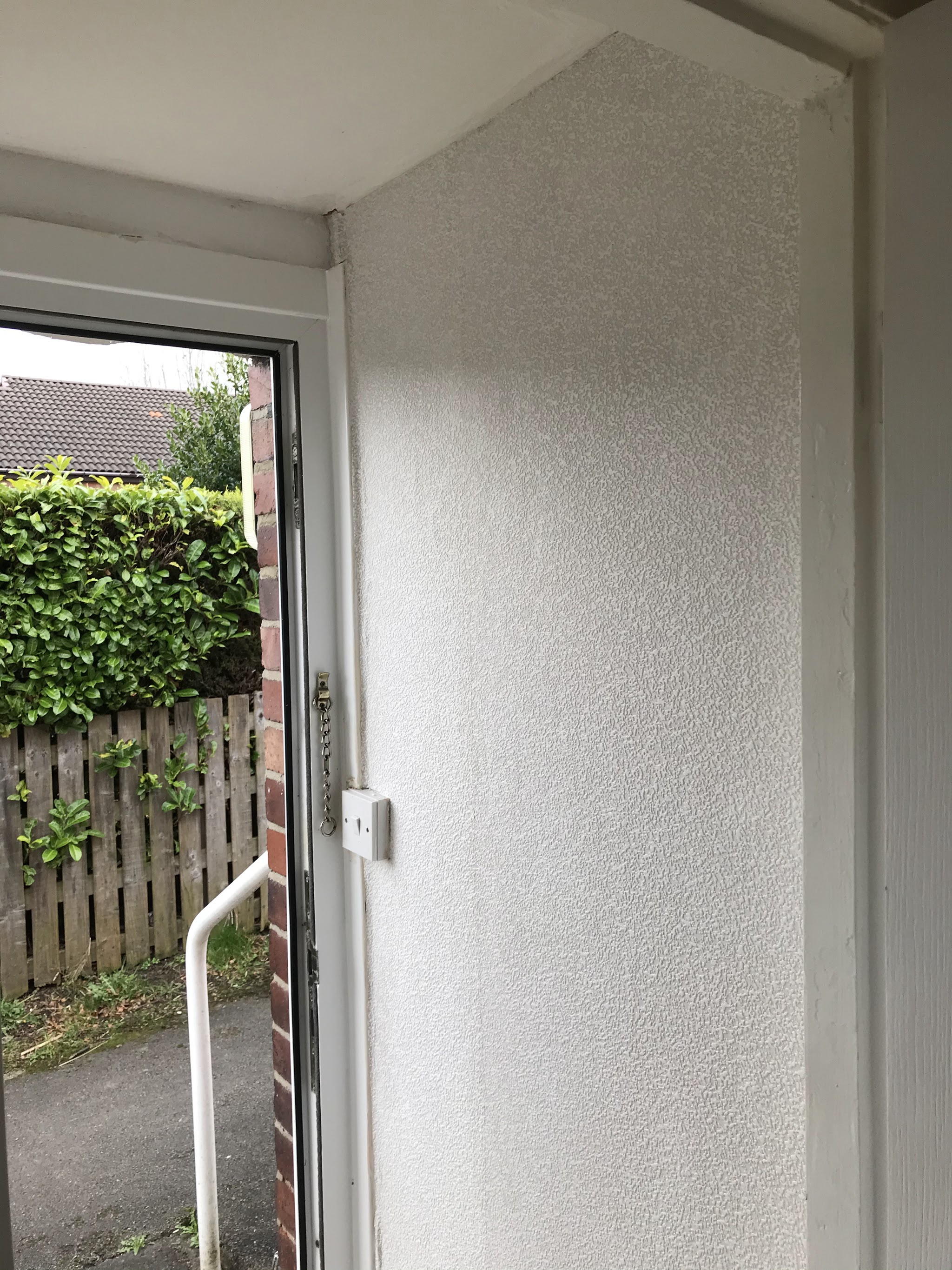 Finished porch with a white textured wall and white door frame, garden hedge outside